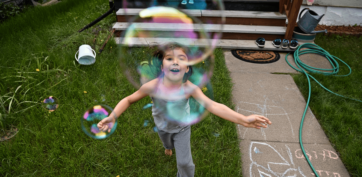 Smiling child playing with colorful bubbles outdoors on a sunny day.